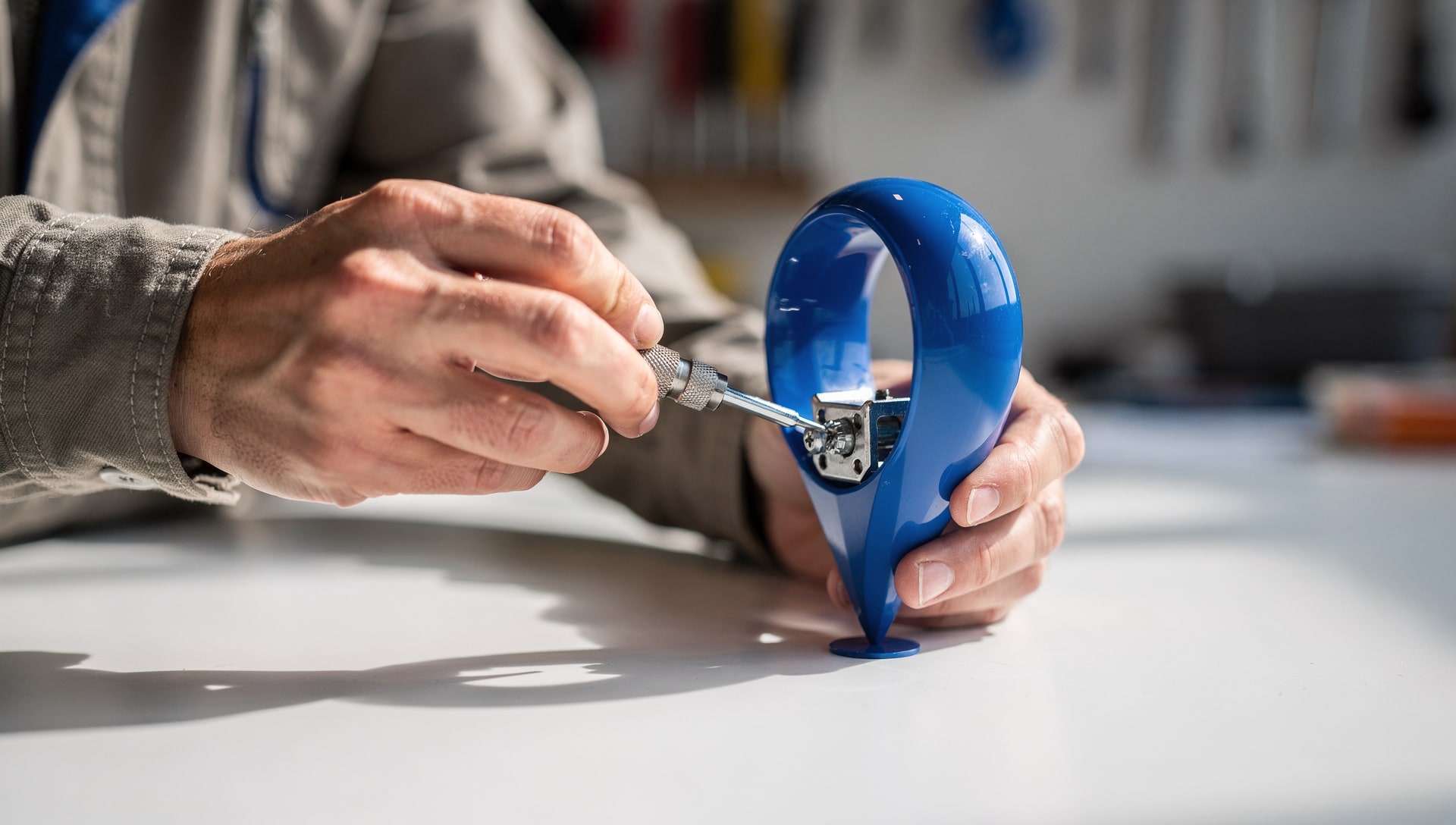 Hands fine-tuning a blue map pin with a precision screwdriver on a workbench