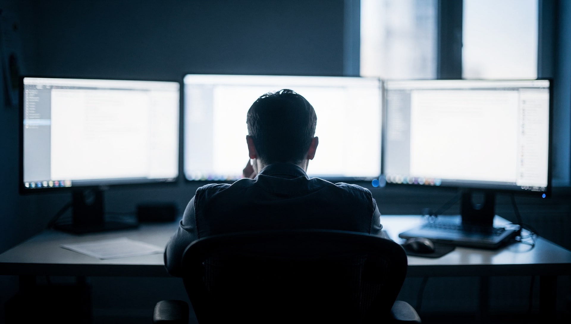 Person facing several glowing software dashboards on multiple monitors